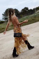 Pollera midi de cuero con estampado marmolado en tonos marrones y mostaza, de corte asimétrico con detalles de largos flecos colgantes en el borde inferior.