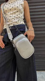 Bandolera compacta color rojo con textura de cuero, correa regulable y desmontable con diseño de rayas rojas y blancas. Cuenta con bolsillos frontales y cierre, interior forrado en tela.