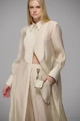 Camisa larga semitransparente de diseño fluido, con cuello clásico, mangas largas con puños anchos y detalle de nervaduras verticales en el frente. Presenta una caída ligera y sofisticada.