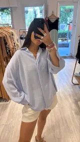 Camisa oversize de manga larga, color celeste con rayas blancas finas, cuello clásico y botones frontales.
