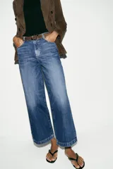 Jeans de tiro alto con pernera ancha y corte cropped. Presenta diseño de cinco bolsillos, cierre frontal con cremallera y botón, e incluye un cinturón oscuro con hebilla metálica.