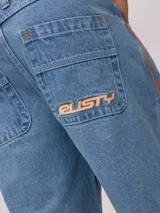 Bermuda de jean de mezclilla negra con efecto lavado, corte recto y costuras en contraste de hilo blanco. Presenta un parche bordado con el logo "Rusty" en color celeste en el bolsillo trasero derecho.
