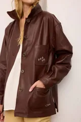 Chaquetón de cuero oversized color marrón, con corte recto, cuello camisero y cierre frontal de botones. Presenta bolsillos delanteros con bordados inspirados en la costa atlántica.