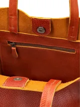 Cartera tipo shopper de cuero color terracota, sin forro y con terminaciones al corte. Cuenta con bolsillo interior con cierre.