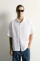 Camisa regular fit confeccionada en tejido de lino, color blanco, con cuello solapa, manga corta y cierre frontal de botonadura.