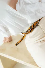 Cinturón fino de cuero marrón con hebilla metálica dorada y ojales.