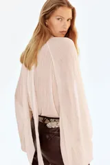 Blusa oversized de tejido liviano con efecto arrugado, cuello elevado drapeado con abertura en V, frunces frontales y tiras largas en la espalda. Presenta mangas globo largas de corte raglán con costura interior abierta y puños elásticos.