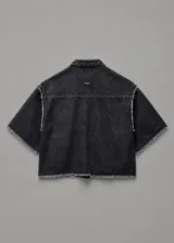 Chaqueta de denim negro con lavado ácido, cuello mao, mangas cortas, cierre frontal con botones metálicos y un bolsillo aplicado en el pecho. Presenta detalles de terminaciones desflecadas en el cuello, mangas y ruedo.