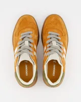 Championes deportivos Coolway modelo Goal, color naranja óxido con detalles en blanco, marrón y verde. Confeccionados en serraje suave con lengüeta preformada de piel, forro interior en piel, cordones planos de algodón bicolor intercambiables y suela flexible de goma y caucho.