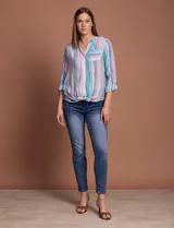 Blusa de gasa con estampado de rayas verticales en tonos celestes, violetas y blancos. Presenta cuello mao con escote en V, cierre frontal con botones, bolsillo aplicado en el pecho y mangas largas con presilla para regular el largo. El diseño incluye un nudo en la parte inferior delantera.