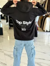 Canguro negro oversize con capucha y gran estampado blanco en la espalda con el texto "Top Style", "Dream big. Work hard. Make it real.", "SINCE 2021" y un código de barras.