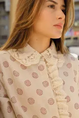 Camisa color crema con estampado de círculos marrones, cuello con volados y puntilla, y cierre frontal con botones.