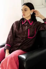 Camisa de broderie color chocolate con detalles de bies en color fucsia en el cuello, bolsillos y puños. Presenta un corte amplio, estilo relajado, mangas largas y cierre frontal con botones.