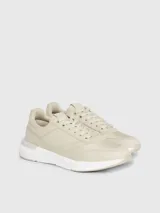 Zapatillas deportivas de mujer Calvin Klein, color beige claro, con cordones y suela gruesa blanca. Presentan una combinación de materiales que incluye piel natural y ecológica, con paneles de malla y detalles de monograma sutil en el lateral.