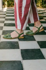 Sandalias de cuero color celeste, con punta cerrada, flecos frontales y detalle de estribo metálico dorado. Tienen tira ajustable al tobillo y suela plana con pequeño taco.