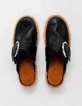Mules de cuero negro con hebilla plateada y suela color madera.