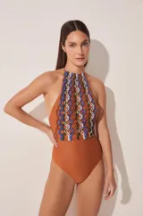 Traje de baño enterizo color ladrillo, con escote halter y espalda descubierta. Presenta un panel de macramé multicolor en el frente.