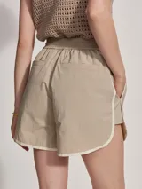 Short deportivo color beige con ribetes blancos, cintura elastizada y corte holgado.