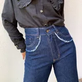 Pantalón jean de tiro alto en color azul oscuro, con bolsillos delanteros redondeados con detalles deshilachados.