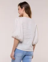 Blusa color beige confeccionada en lino, con escote en V pronunciado y cierre frontal de múltiples lazos para atar. Presenta mangas abullonadas tres cuartos con puños elásticos y corte relajado.