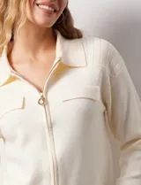 Cardigan de tejido punto color crema, con cuello tipo solapa, cierre frontal completo con tirador circular metálico y dos bolsillos de parche simulados en el frente. Presenta detalles de canalé en los hombros.