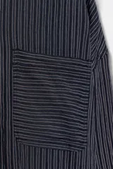 Camisa fluida de corte oversize confeccionada en mezcla de viscosa, con diseño de rayas verticales finas en tono beige sobre fondo blanco. Presenta cuello solapa, cierre frontal con botones, manga larga con puños y un bolsillo de plastrón en el pecho.