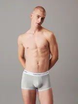 Pack de tres bóxers tipo trunk Calvin Klein de talle bajo, confeccionados en mezcla de algodón y elastano. Incluye uno en color azul, uno gris y uno negro con monogramas estampados. Todos cuentan con cinturilla elástica blanca con el logo de la marca.