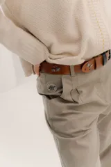 Pantalón tipo sastrero color beige, de tiro medio, con pinzas delanteras, bolsillos delanteros con pin bordado BYF y bolsillos traseros tipo vivo.