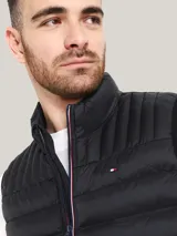 Chaleco acolchado de nailon color negro, con cuello alto, cierre frontal de cremallera con detalles distintivos de la marca y bolsillos laterales con cierre. Presenta el logo de Tommy Hilfiger bordado en el pecho.