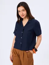Camisa de manga corta color blanco, confeccionada en mezcla de viscosa, poliamida y lino, con cuello camisero y cierre frontal de botones.