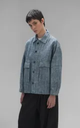 Campera oversize crop de denim rígido en tono azul con trama única, cuello camisero, cierre frontal con botones oscuros y bolsillos delanteros con solapa.