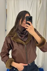 Campera bomber corta de cuero ovino marrón con detalles en napalan coñac y forro interior. Presenta cuello solapa, cierre frontal con cremallera de doble sentido, bolsillos laterales ribeteados, mangas largas con detalles de pasamanería cruzada y puños de piel sintética.