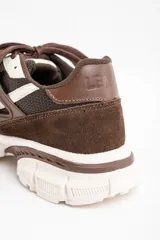 Zapatilla urbana de diseño robusto, confeccionada en una combinación de malla, gamuza y detalles en cuero sintético. Presenta una paleta de colores en tonos chocolate y crema, con suela dentada de goma de gran volumen.