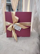 Caja de regalo artesanal color bordó con moño dorado, diseñada como experiencia de lujo para presentar un conjunto de lencería. Incluye elementos de regalo adicionales como perfume, rosa natural y dulces.