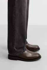 Bota tipo Chelsea de piel color marrón oscuro, con paneles elásticos laterales, tirador trasero y suela de goma con ligero tacón.