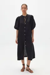 Vestido midi negro confeccionado en lino, con cuello mao, mangas abullonadas hasta el codo y cierre frontal con botones de nácar.