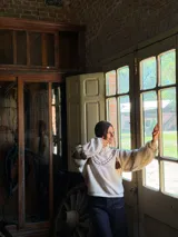 Buzo de punto color crema con diseño oversize, cuello redondo y mangas largas abullonadas. Presenta detalles de costuras decorativas en contraste y apliques de flecos colgantes en la parte frontal y mangas.