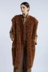 Chaleco largo reversible de diseño versátil. Por un lado, presenta una textura de peluche sintético en color marrón, y por el otro, un acabado liso. Cuenta con cierre frontal de botones y corte recto.