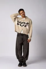 Campera tejida de punto con cierre frontal completo y cuello polo. Presenta un diseño de franja horizontal ancha en color crema con estampado gráfico oscuro sobre una base de color marrón. Posee puños y ruedo acanalados, con un pequeño parche de marca en el puño izquierdo.