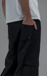 Pantalón cargo de corte oversize y silueta estructurada, confeccionado en microfibra pesada con leve elasticidad. Presenta cintura elástica con cordón de ajuste externo, cierre frontal con botón metálico, bolsillos laterales y bolsillos cargo de gran tamaño con tapa y broches a presión.
