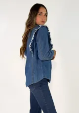 Camisa de denim azul oscuro con cuello clásico, cierre frontal de botones y detalle de volados en los hombros.