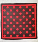 Pañuelo cuadrado de tela con estampado de lunares rojos sobre fondo marrón, con borde en contraste.