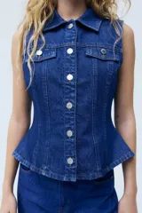 Chaleco de denim azul rígido de algodón, con cuello camisero, cierre frontal de botones metálicos, bolsillos con solapa en el pecho y detalle de peplum en la parte inferior.