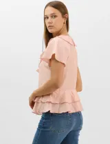 Blusa de satén color rosado con acabado texturizado, escote en V con volados, mangas cortas acampanadas y diseño péplum de doble nivel en la parte inferior.
