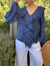 Camisa de lino azul marino con volados en cascada a lo largo del frente y en los puños de las mangas largas. Presenta un escote en V con un botón de nácar visible.