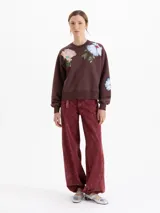 Buzo de corte oversize color marrón chocolate, con cuello redondo y diseño estampado de flores en la parte frontal. Presenta mangas largas con puños ajustados.