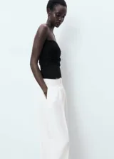 Pantalón de traje tiro medio, color blanco, de diseño recto y largo, con cierre delantero de botón, gancho y cremallera, detalle de pinzas y dos bolsillos laterales.