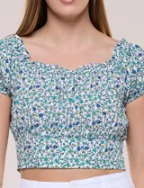 Top corto estampado con diseño floral en tonos azules y verdes sobre fondo blanco, con escote corazón fruncido con elástico, mangas cortas abullonadas y pretina ancha bajo el busto.