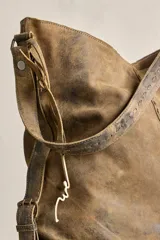 Cartera tote de cuero suave color marrón con efecto envejecido, cuerpo blando, caída relajada, correa ancha fija al hombro y costuras decorativas pespunteadas.