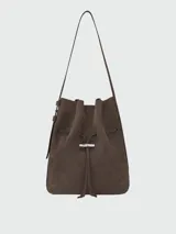 Cartera tipo bucket bag de hombro Longchamp modelo Le Roseau Velvety M, confeccionada en cuero marrón con textura de gamuza. Cuenta con correa de hombro ajustable y detalle de cierre de barrita metálica con el distintivo de la marca.